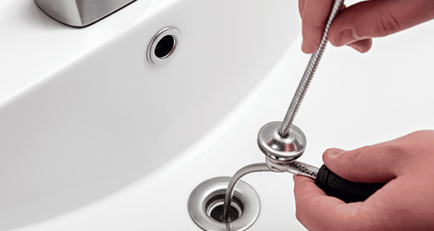 Feeding a hand drain snake auger into bathroom sink drain to clear a stubborn clog